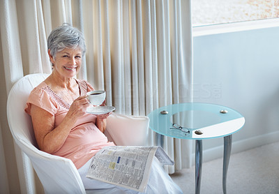 Happy senior lady with newspaper drinking coffee at home