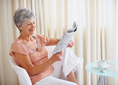 Relaxed happy senior woman reading newspaper at home