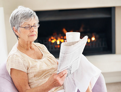 Senior woman reading a newspaper by the fireplace