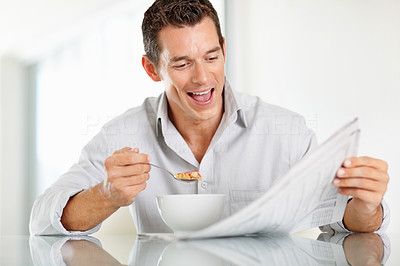 Happy middle aged man reading newspaper while having breakfast