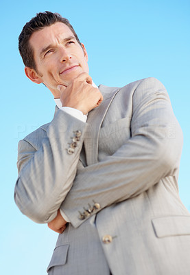 Smart middle aged business man with hand on chin against sky