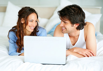 An affectionate couple lying on bed with a laptop