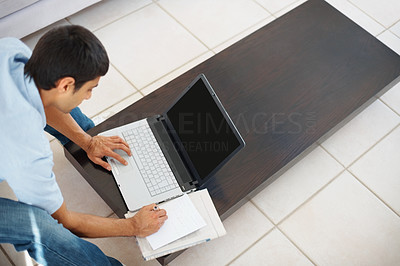 Top view of a man making notes while using laptop at home