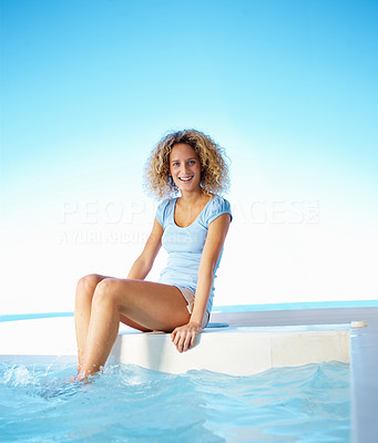 Happy young woman sitting by swimming pool and smiling