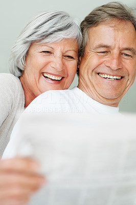 Senior couple smiling together while reading newspaper