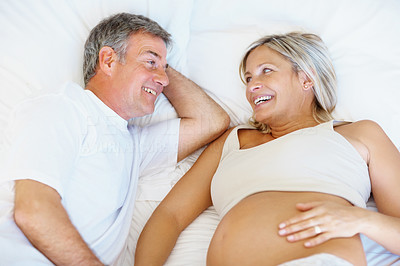 Happy mature pregnant couple lying in bed