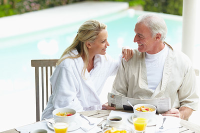 Mature couple having a chat at breakfast table by swimming pool
