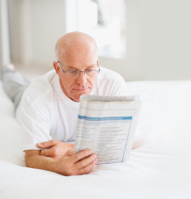 Senior man reading a newspaper on bed at home