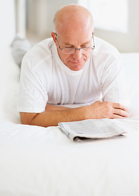 An old senior man reading a newspaper on bed at home