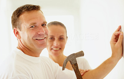 Happy man hammering a nail into the wall with wife at the back