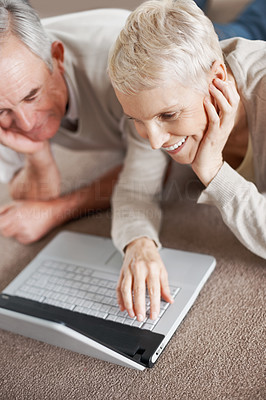 Senior couple using a laptop while lying on the floor