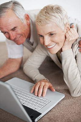 Senior couple using a laptop while lying on the floor