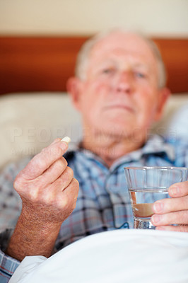 Blur image of a senior man holding a pill in bed