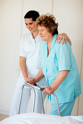Senior woman being helped by a nurse to walk on a walker