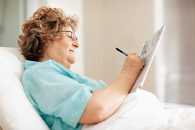 Happy old woman solving a crossword puzzle in bed