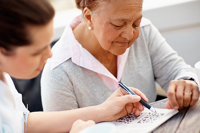 Old woman being helped by a nurse to solve a crossword puzzle