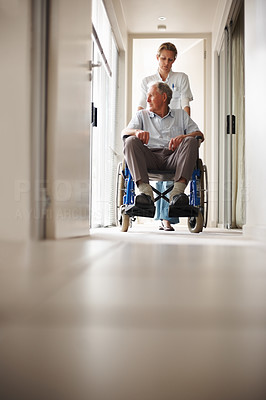 Nurse pushing an old man on a wheelchair at the corridor