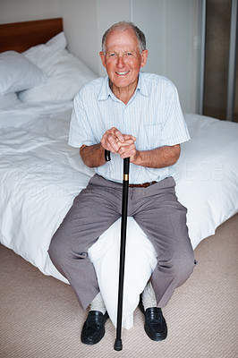 Happy elderly man at the edge of the bed with a walking stick