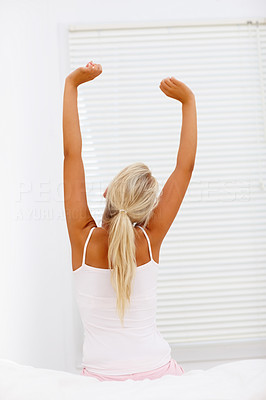 Rear view of tired woman stretching her arms in bed