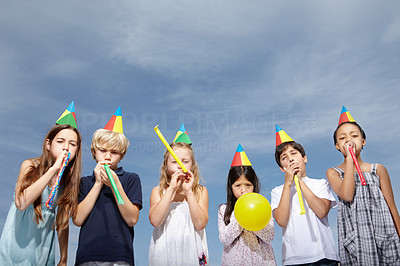 Multi ethnic kids blowing party horns against sky - copyspace
