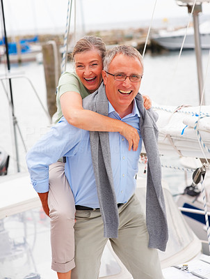 Happy mature man piggybacking his wife on a sailboat voyage