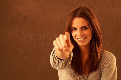 Beautiful young woman pointing at you against brown background