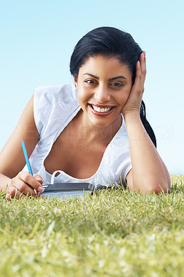 Young woman lying on a meadow and writing a diary