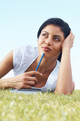 Thoughtful lady lying on grass with a notebook