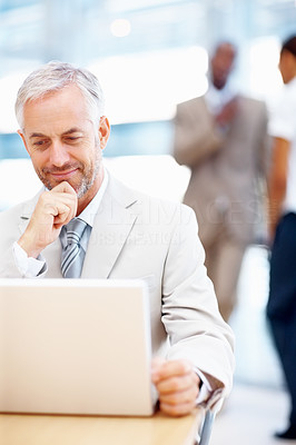 Confident business man working on a laptop with staff at the back