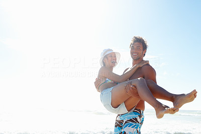 Handsome young man carrying his girlfriend in his arms at the beach
