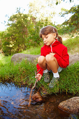 Cute small girl sitting by a stream with a stick in her hand, at the forest