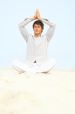 Man meditating with his hands joined above his head at a beach