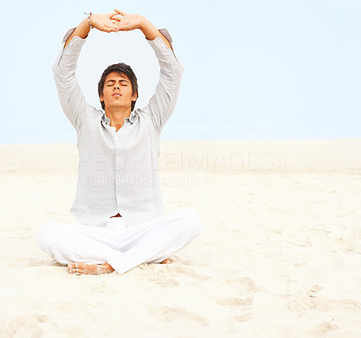 Man meditating with his hands together above his head at a beach