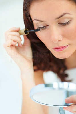 Charming woman looking into the mirror and using mascara