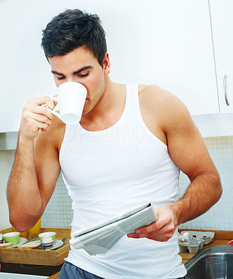 Handsome young man reading a newspaper and drinking tea
