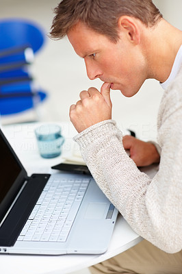 Tensed young man with his finger in his mouth and working on a laptop