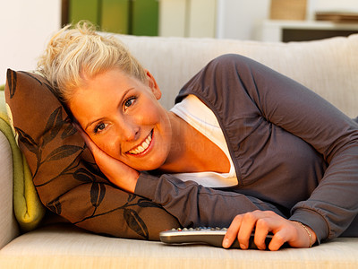 Cute happy lady resting on a couch and holding remote