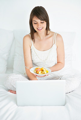 Young woman using laptop while eating fruit salad