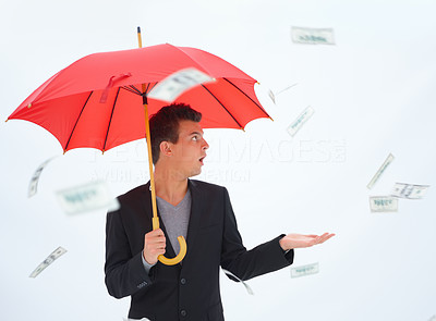 Business man holding red umbrella and looking at money in the air