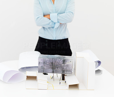 Female architect standing against white background with a house model