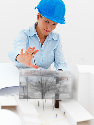 Smiling female architect standing against white background with a house model