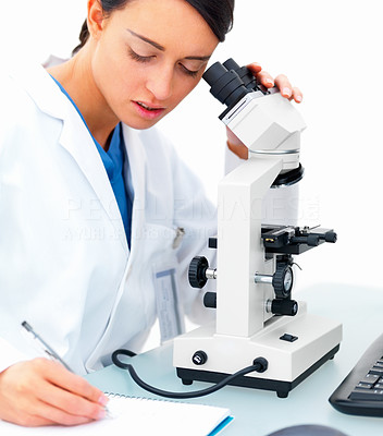 Female researcher looking into microscope and making notes