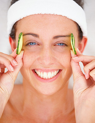 Closeup portrait of a smiling young woman holding cucumber slices by eyes