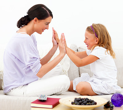 Mother with daughter sitting on sofa and playing clapping game