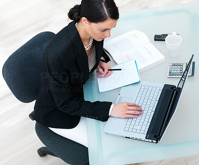 Young businesswoman working on laptop with books, calculator, notebook, cellphone and cup on table