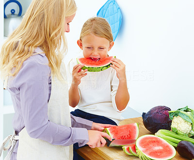 Mother with her daughter in kitchen eating watermelon