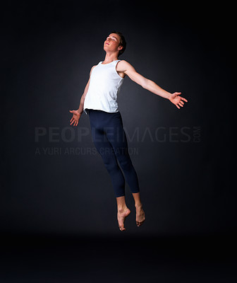 Graceful male ballet dancer performing against black background