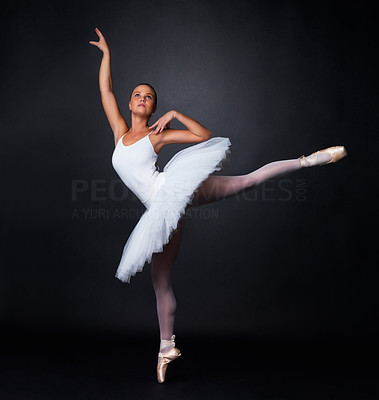 Pretty young ballerina performing against black background