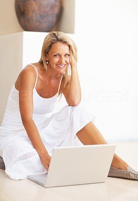 Smiling mature woman sitting on floor using laptop