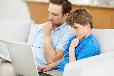 Little boy using laptop with his father reading newspaper on couch